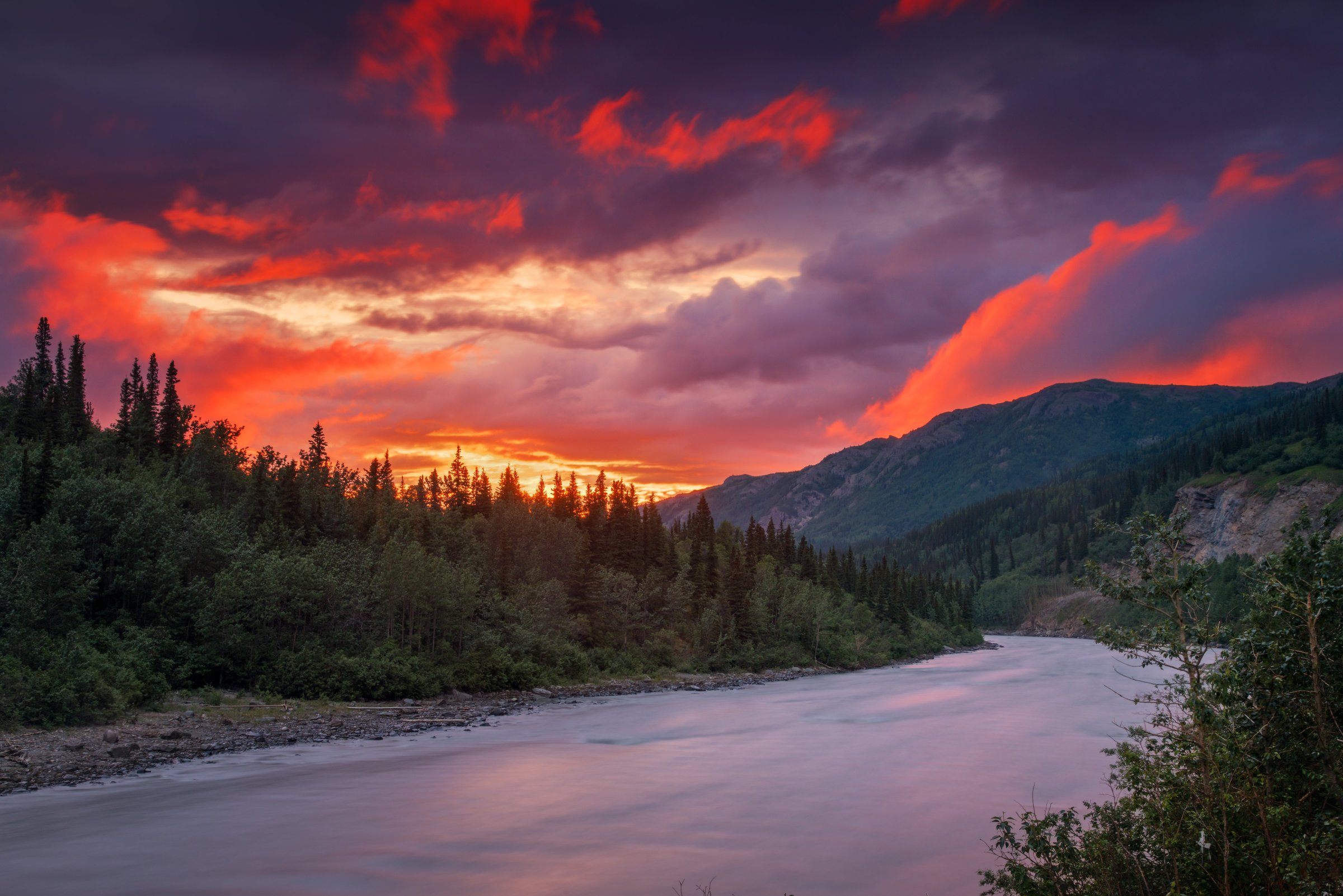 Alaska river landscape at sunset, deep red sky over dark forest and river