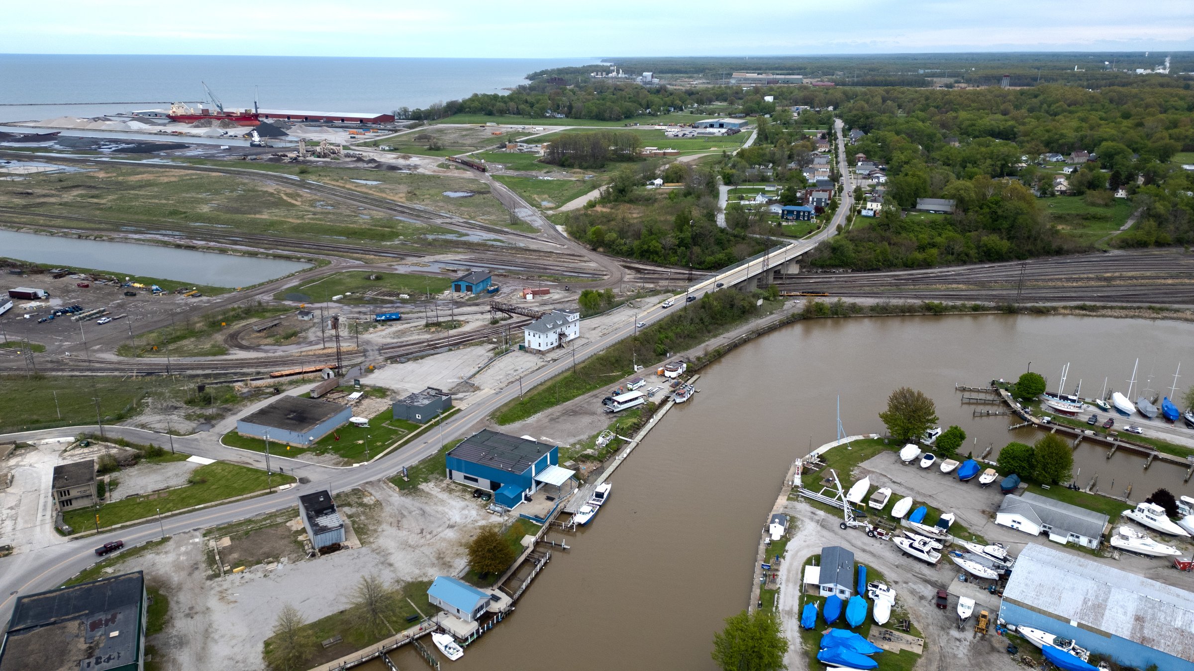 Aerial view of a Rust Belt harbor town on Lake Erie with docked freighters, a bridge, and mixed industrial and residential areas